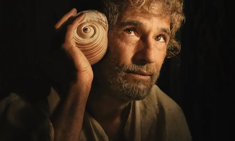 Rodrigo Santoro segura uma concha e observa o horizonte em cena de O Filho de Mil Homens, novo filme da Netflix dirigido por Daniel Rezende.