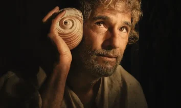 Rodrigo Santoro segura uma concha e observa o horizonte em cena de O Filho de Mil Homens, novo filme da Netflix dirigido por Daniel Rezende.