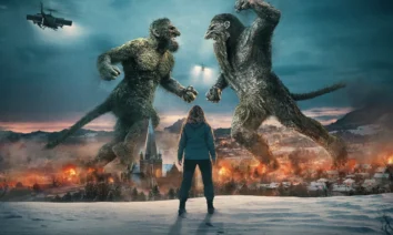 Cena épica de O Troll da Montanha 2, com dois trolls gigantes lutando diante de uma cidade em chamas e Ine Marie Wilmann observando de costas.
