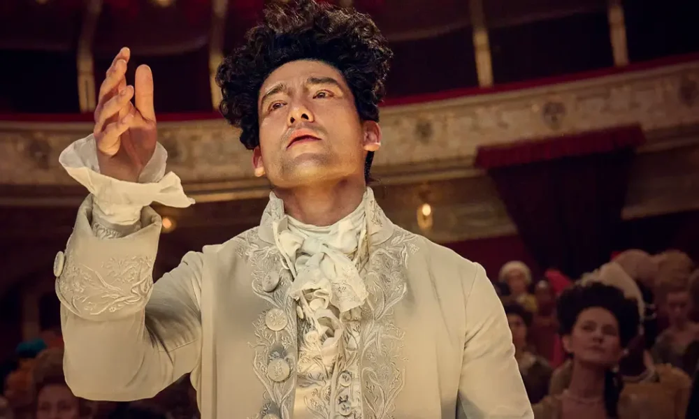 amadeus serie 2025 Will Sharpe como Wolfgang Amadeus Mozart na série Amadeus da Sky TV, vestindo traje de época branco ornamentado do século XVIII em teatro