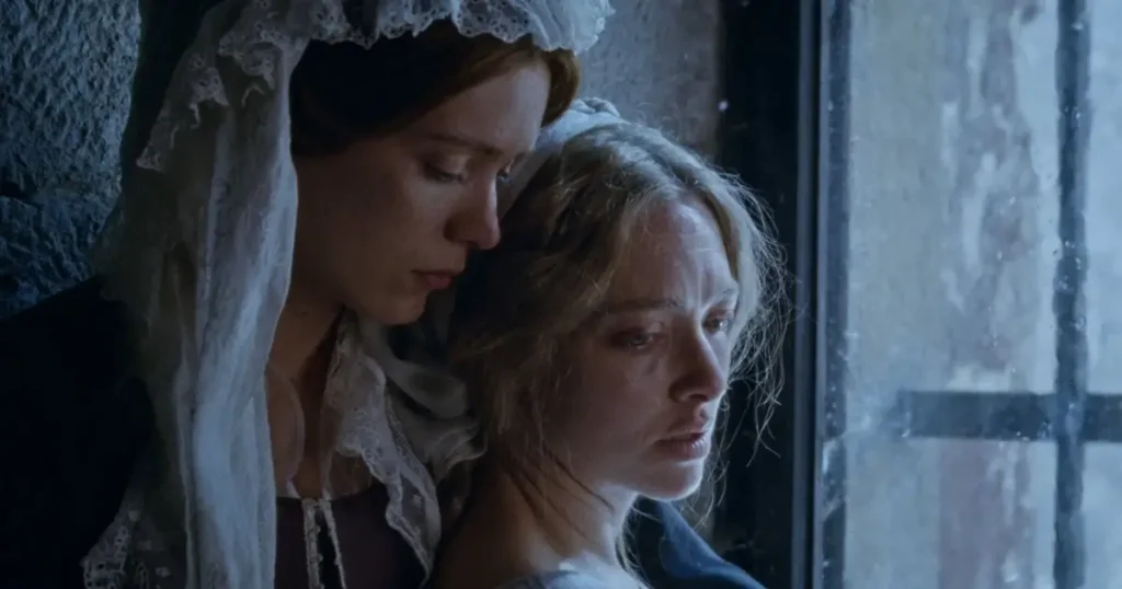 elenco de the testament of ann lee Amanda Seyfried e Thomasin McKenzie em uma cena emocional do filme The Testament of Ann Lee, exibindo a relação entre suas personagens.