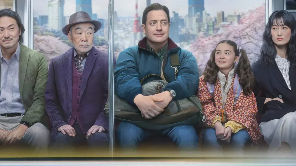 Brendan Fraser e elenco sentados em trem observando cerejeiras em Família de Aluguel (2025), comédia dramática da Disney com lançamento de 2026 no Brasil