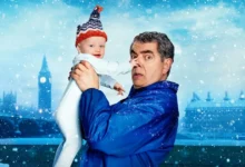 Rowan Atkinson segura um bebê em cena divertida da série Homem x Bebê, da Netflix.