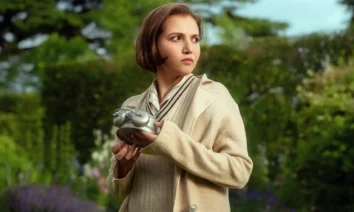 Mia McKenna-Bruce segura um relógio antigo no jardim em cena da série Os Sete Relógios de Agatha Christie, produção original da Netflix.