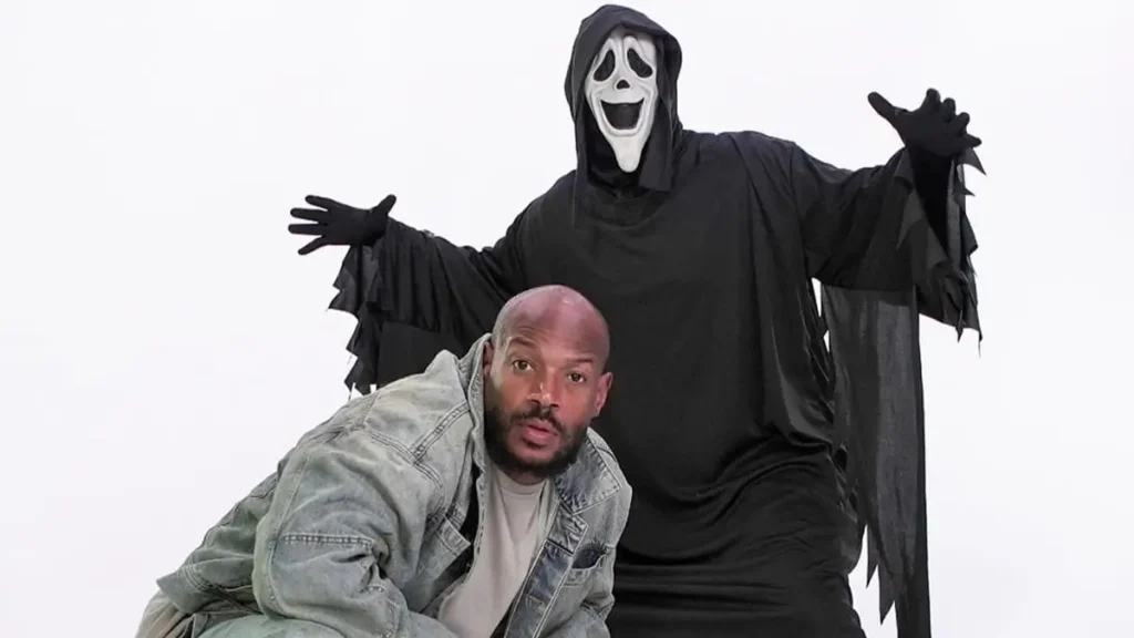 Marlon Wayans na divulgação de Todo Mundo em Pânico 6, com o personagem mascarado ao fundo, filme de comédia que estreia em 11 de junho entre os filmes de 2026.