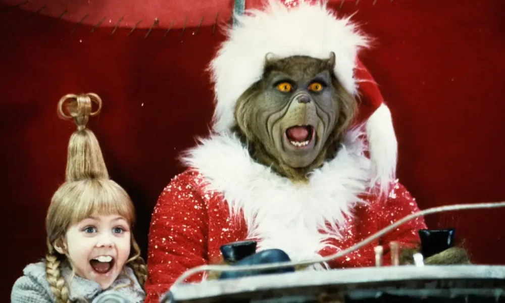 Cena do filme O Grinch (2000) com o Grinch vestido de Papai Noel e Cindy Lou Who sorrindo ao seu lado; imagem utilizada no especial “O elenco de ‘O Grinch’ 25 anos depois”.
