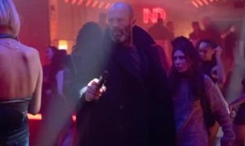 Jason Statham armado em cena do filme Shelter (2026), dirigido por Ric Roman Waugh, dentro de uma boate iluminada.