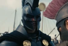 Cena do trailer de A Odisseia (The Odyssey), novo filme de Christopher Nolan, com guerreiro usando armadura e capacete em cenário épico inspirado na Grécia Antiga