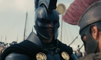 Cena do trailer de A Odisseia (The Odyssey), novo filme de Christopher Nolan, com guerreiro usando armadura e capacete em cenário épico inspirado na Grécia Antiga