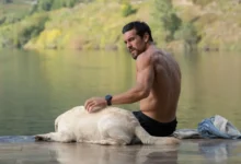 Mario Casas em cena de Agente Zeta, suspense do Prime Video, sentado à beira de um lago ao lado de um cachorro