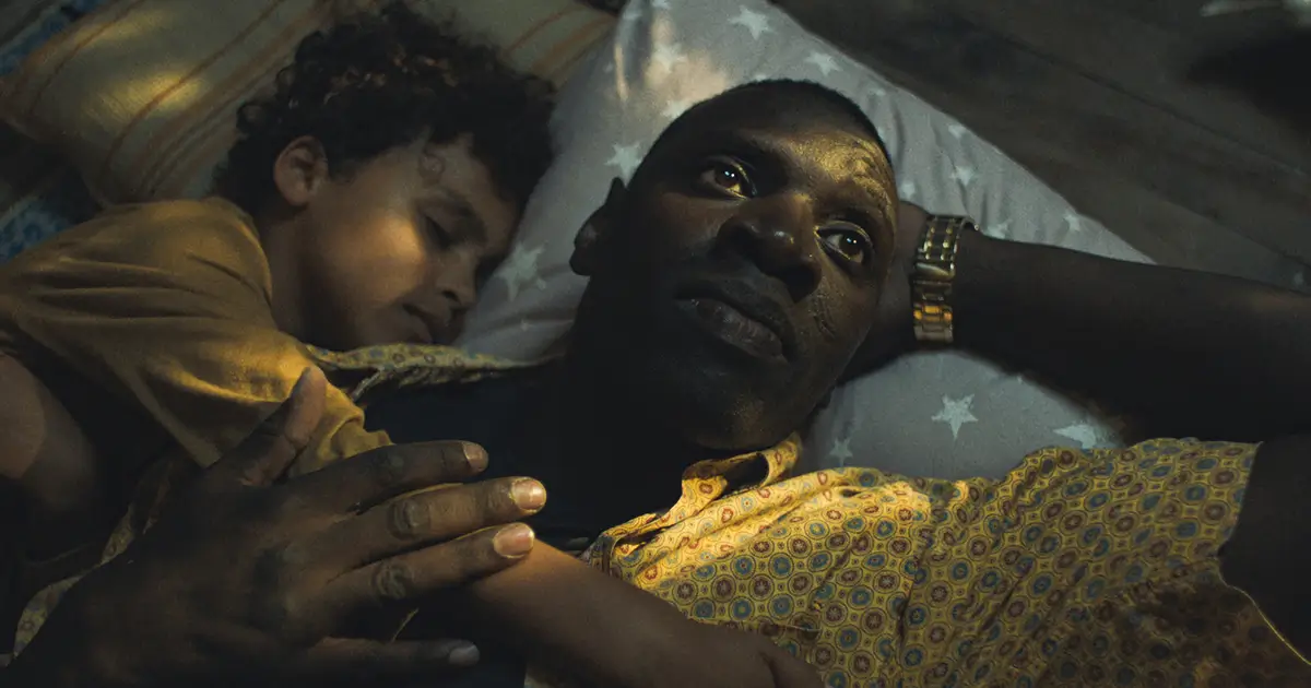 Omar Sy em cena emocional de O Caso dos Estrangeiros, deitado com uma criança
