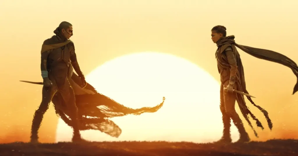 Cena de Duna: Parte 3 (Dune: Part Three) com dois personagens frente a frente em um cenário desértico iluminado por um enorme sol.