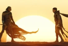 Cena de Duna: Parte 3 (Dune: Part Three) com dois personagens frente a frente em um cenário desértico iluminado por um enorme sol.