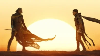 Cena de Duna: Parte 3 (Dune: Part Three) com dois personagens frente a frente em um cenário desértico iluminado por um enorme sol.