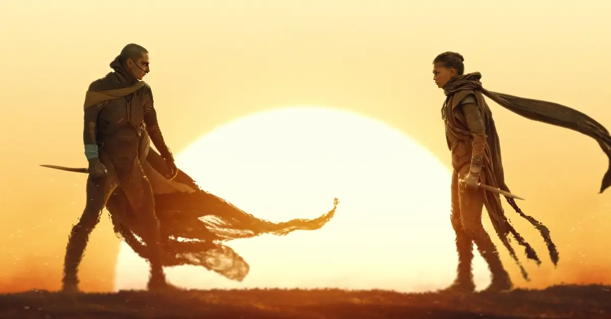 Cena de Duna: Parte 3 (Dune: Part Three) com dois personagens frente a frente em um cenário desértico iluminado por um enorme sol.