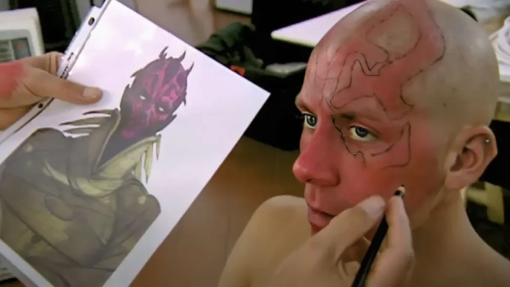 Maquiagem de Darth Maul sendo aplicada em Ray Park com referência de arte conceitual em Star Wars