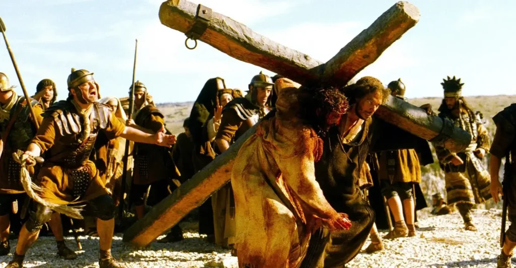 Jim Caviezel como Jesus carregando a cruz em A Paixão de Cristo (2004), um dos filmes mais polêmicos sobre Jesus no cinema