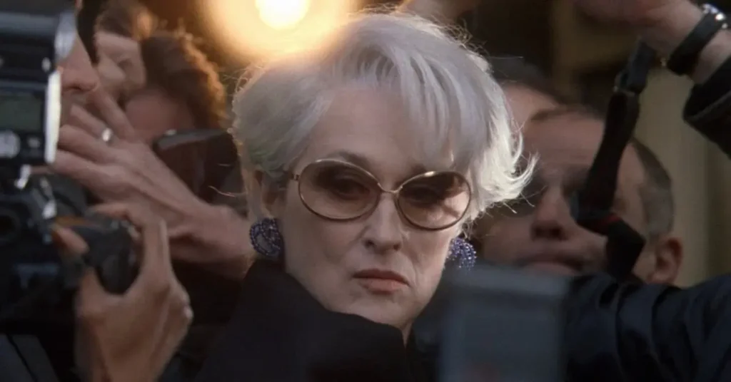 Meryl Streep como Miranda Priestly cercada por fotógrafos em O Diabo Veste Prada, simbolizando o sucesso de bilheteria