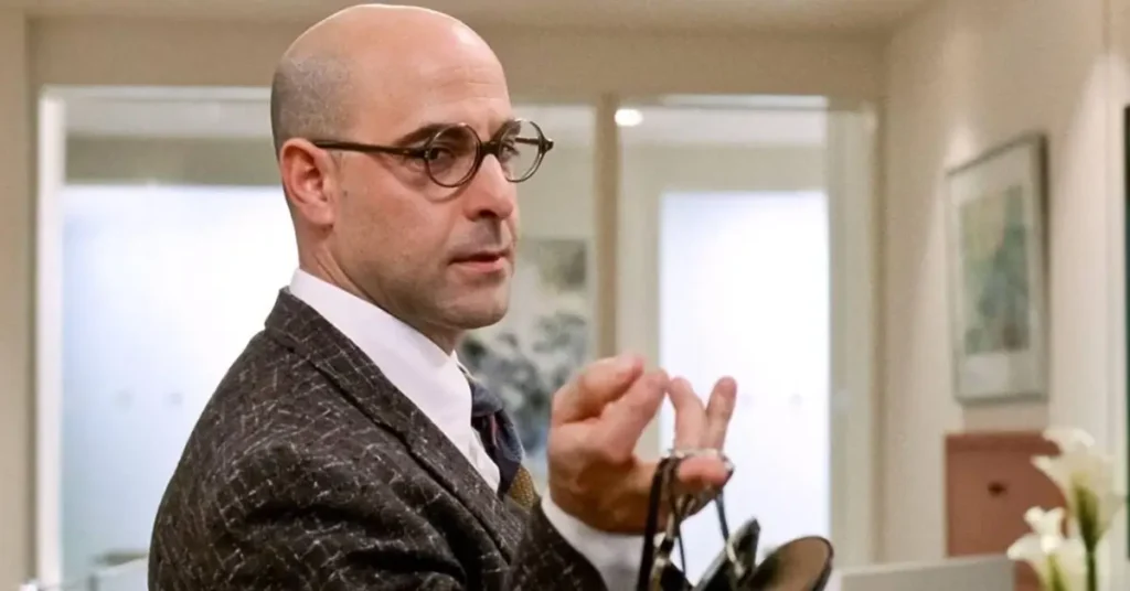 Stanley Tucci como Nigel em O Diabo Veste Prada segurando acessórios de moda na revista Runway, mentor de Andy Sachs