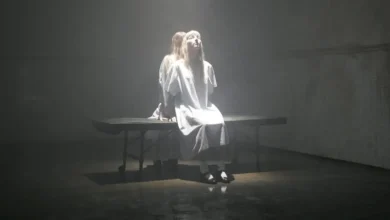 Cena sombria do trailer de Phantasmagoria The Visions of Lewis Carroll com mulher em ambiente hospitalar iluminado, estilo perturbador de Marilyn Manson