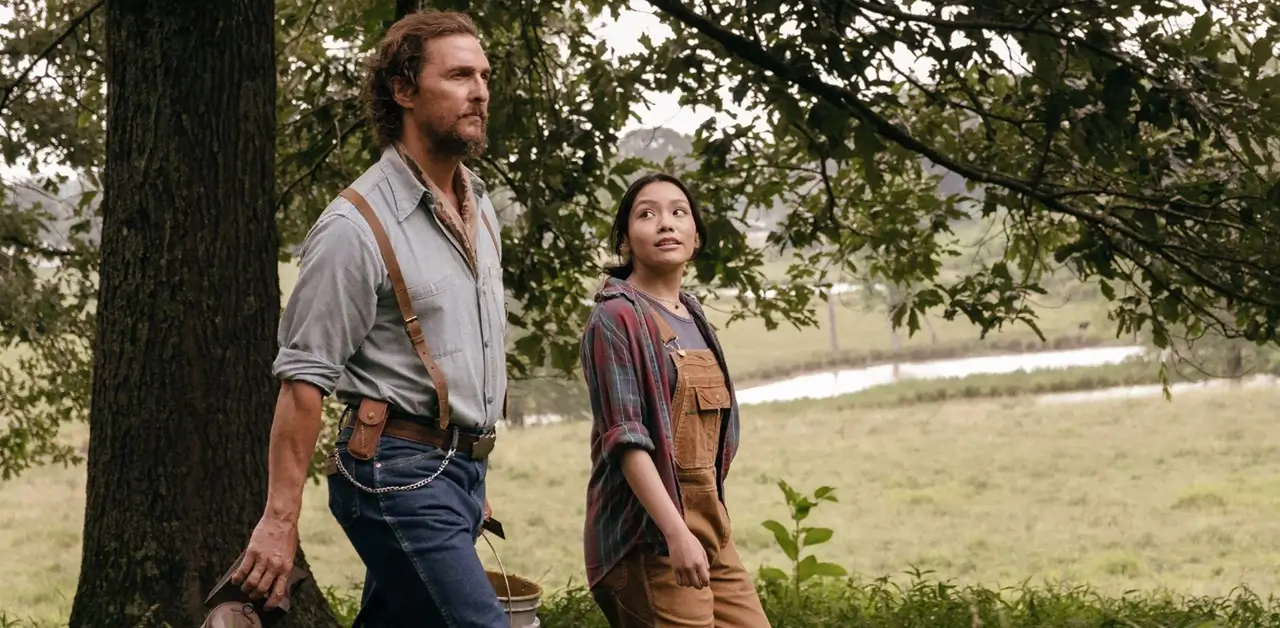 Matthew McConaughey e Angelina LookingGlass em cena do filme Os Rivais de Amziah King, caminhando por uma área rural cercada por árvores