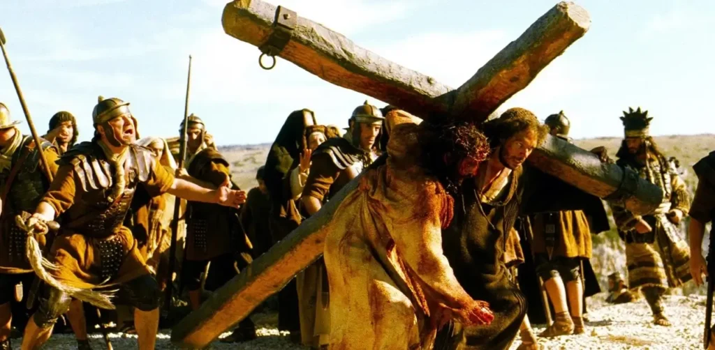 Jim Caviezel carregando a cruz em cena de A Paixão de Cristo, filme marcado por acidentes e incidente com raio durante as gravações