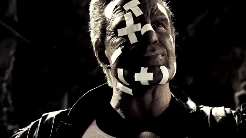 Marv, personagem interpretado por Mickey Rourke em Sin City (2005), com o rosto coberto por curativos em visual inspirado nos quadrinhos de Frank Miller.