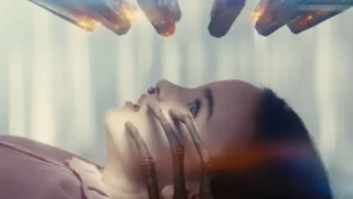 Cena do trailer final de Dia D mostra mulher deitada enquanto uma mão sombria cobre seu rosto em momento de suspense psicológico