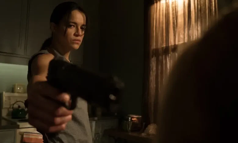 Michelle Rodriguez aponta uma arma em cena tensa do filme Vingança (2016), em ambiente escuro e com clima de suspense.