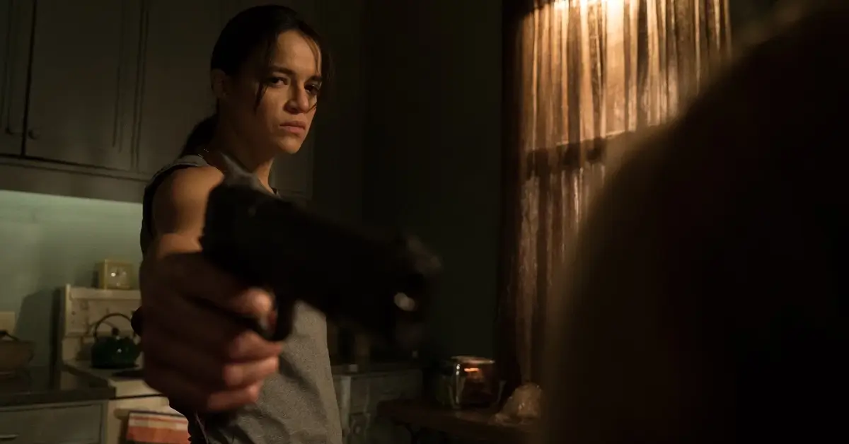 Michelle Rodriguez aponta uma arma em cena tensa do filme Vingança (2016), em ambiente escuro e com clima de suspense.