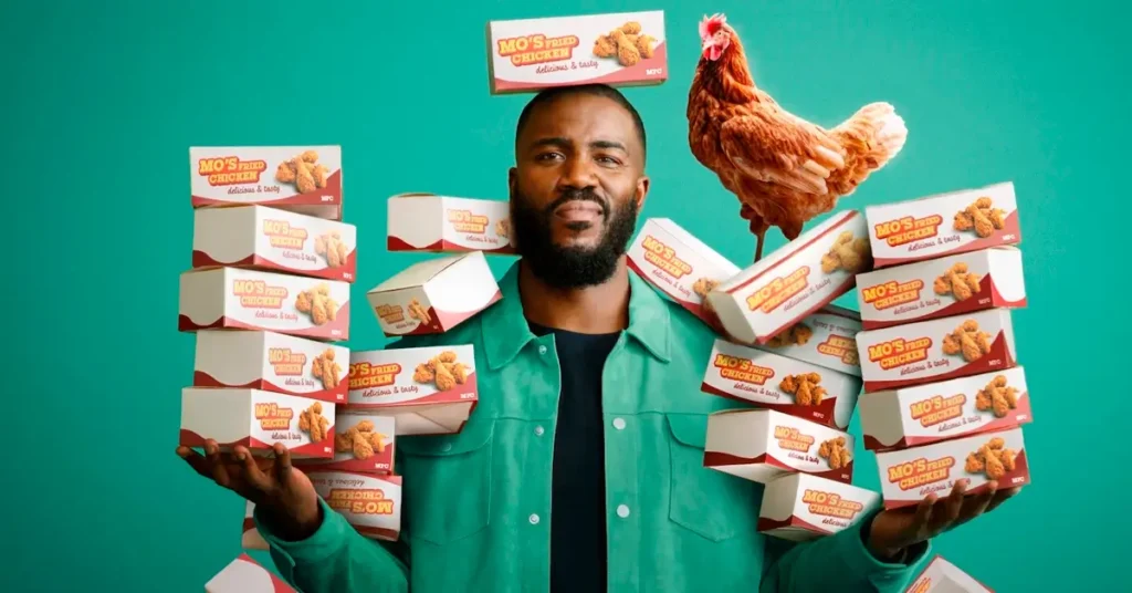 Mo Gilligan cercado por caixas de frango frito em cena do documentário Frango: A Conspiração do Fast-Food.