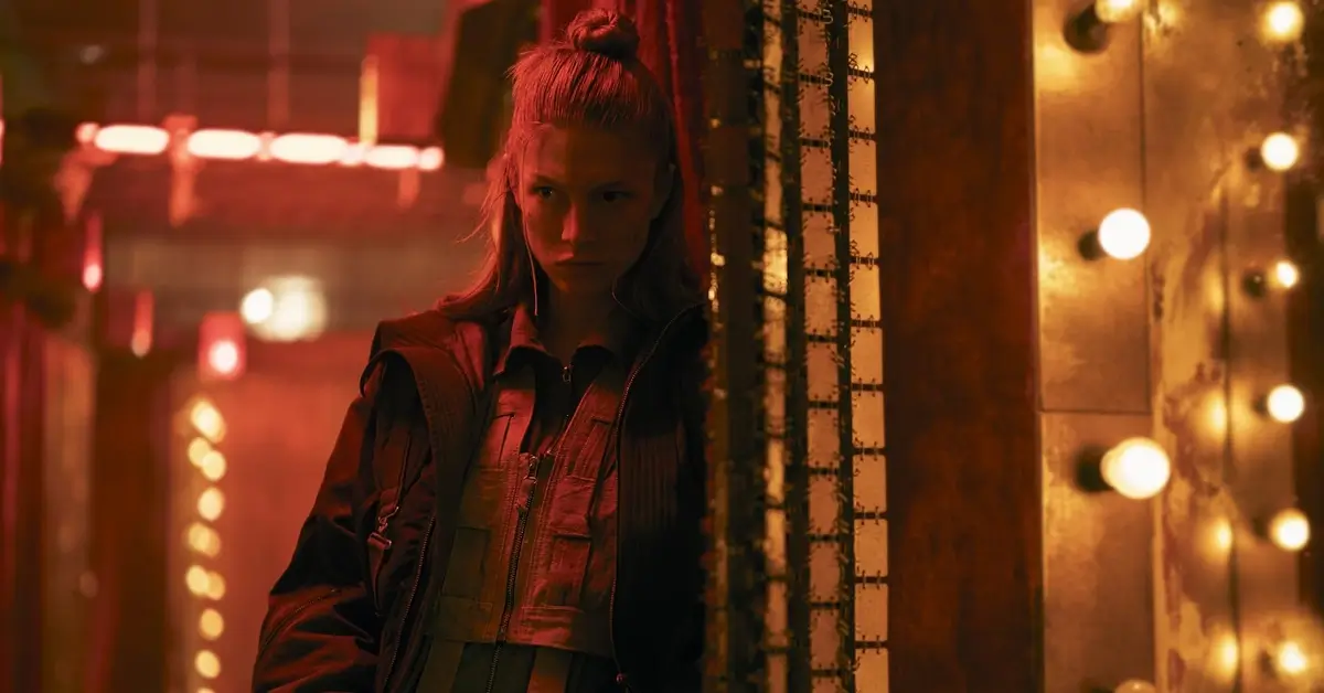 Hunter Schafer como Cora em Blade Runner 2099 (2026), em cenário futurista iluminado por luzes vermelhas e amarelas.