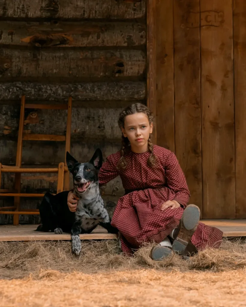 Laura Ingalls ao lado do cão Jack em frente à casa da família na série Uma Casa na Pradaria