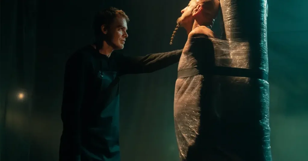 Dexter Morgan, interpretado por Michael C. Hall, observa um homem preso a uma estrutura coberta por plástico em uma cena de tensão de <em>Dexter: Ressurreição</em>, destacando o lado sombrio do personagem na segunda temporada.