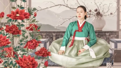 Son Ye-jin interpreta Lady Cho em Escândalo e Intriga (The Scandal), nova minissérie coreana da Netflix ambientada na era Joseon; a atriz aparece sentada em um cenário tradicional cercado por flores vermelhas.