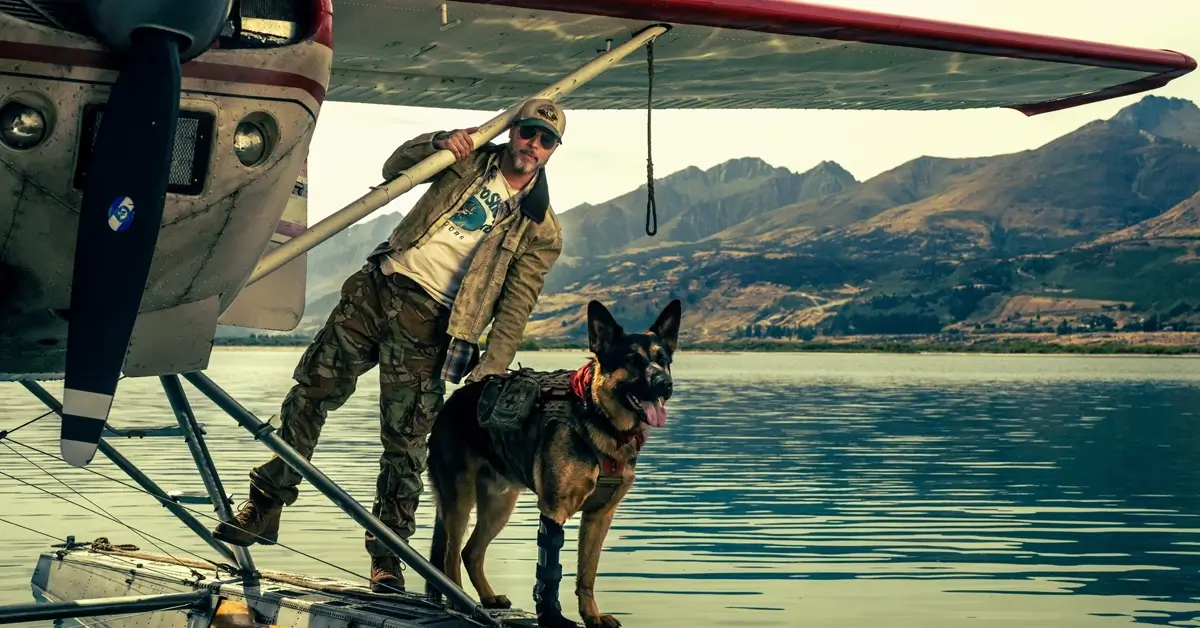 Brad Pitt em Coração Selvagem (2026) ao lado de um cão durante uma missão em um hidroavião sobre um lago cercado por montanhas.