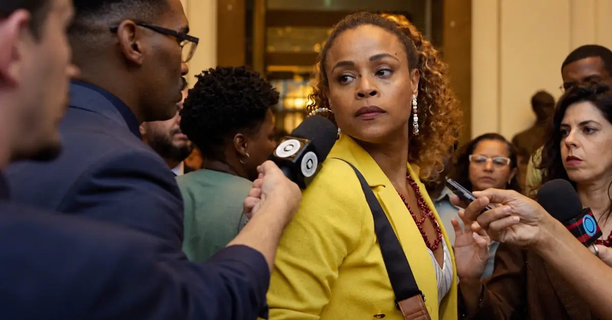 Roberta Rodrigues na segunda temporada de Cidade de Deus: A Luta Não Para, cercada por jornalistas durante uma entrevista.