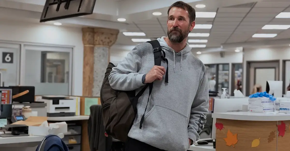 Cena de divulgação da 3ª temporada de The Pitt mostra um médico chegando ao pronto-socorro do hospital com uma mochila nas costas, enquanto o ambiente de atendimento aparece ao fundo.