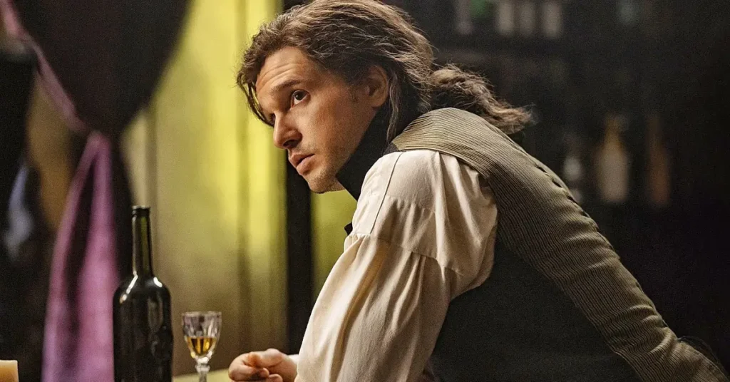 Kit Harington como Sydney Carton em uma cena da minissérie Um Conto de Duas Cidades (A Tale of Two Cities), do MGM+, sentado em um ambiente de época enquanto olha para trás, usando roupas características do século XVIII