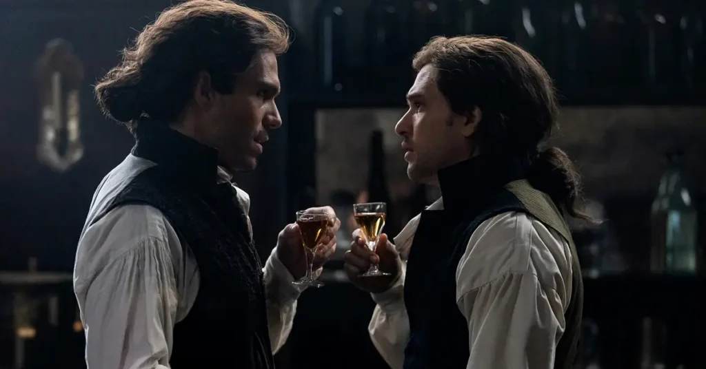 François Civil como Charles Darnay e Kit Harington como Sydney Carton em cena da minissérie Um Conto de Duas Cidades (A Tale of Two Cities), do MGM+, com os dois personagens conversando enquanto seguram taças em um ambiente de época