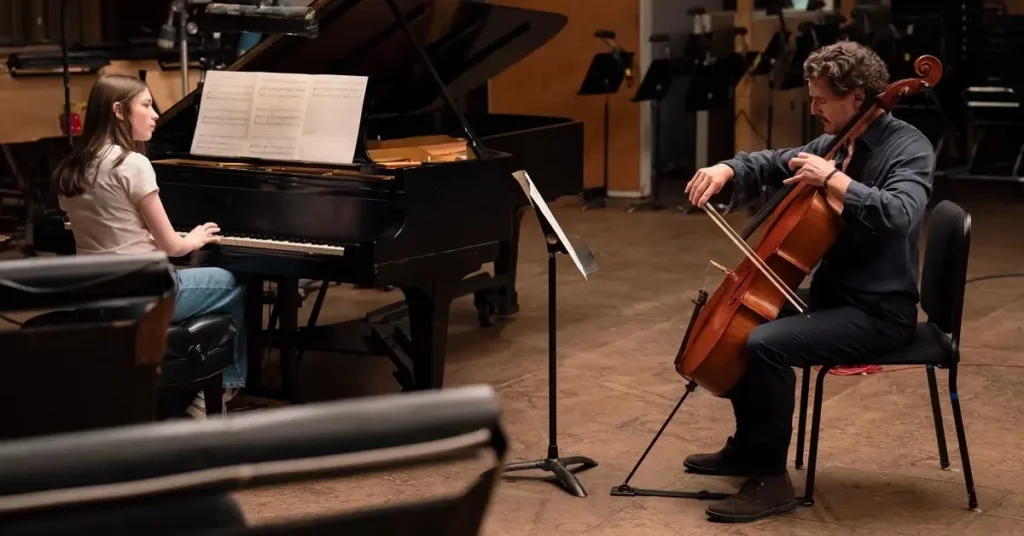 Pedro Pascal como Alex Serian tocando violoncelo ao lado de uma pianista em cena de Behemoth! (2026), possível candidato ao Oscar 2027.