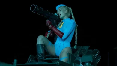 Mel Jarnson como Cammy, com traje azul e luvas vermelhas, empunha uma arma em cena de Street Fighter (2026).