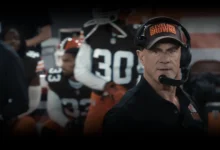 Christopher Meloni como o técnico Danny Roarke, usando boné do Cleveland Browns e headset à beira do campo na série The Land: Além do Jogo (2027).