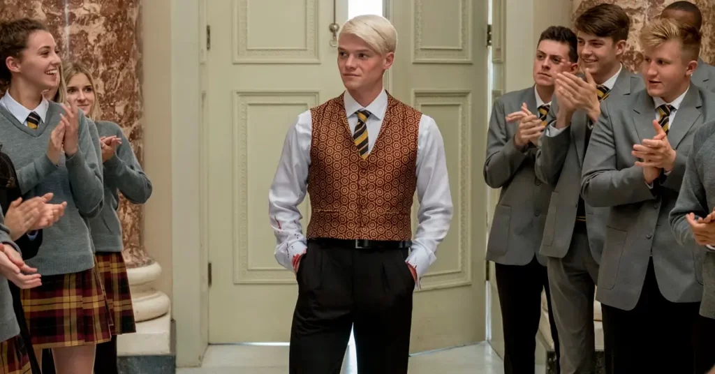 Tom Rhys Harries em cena do filme Escola da Morte (2018), ao lado de estudantes uniformizados em um ambiente escolar.